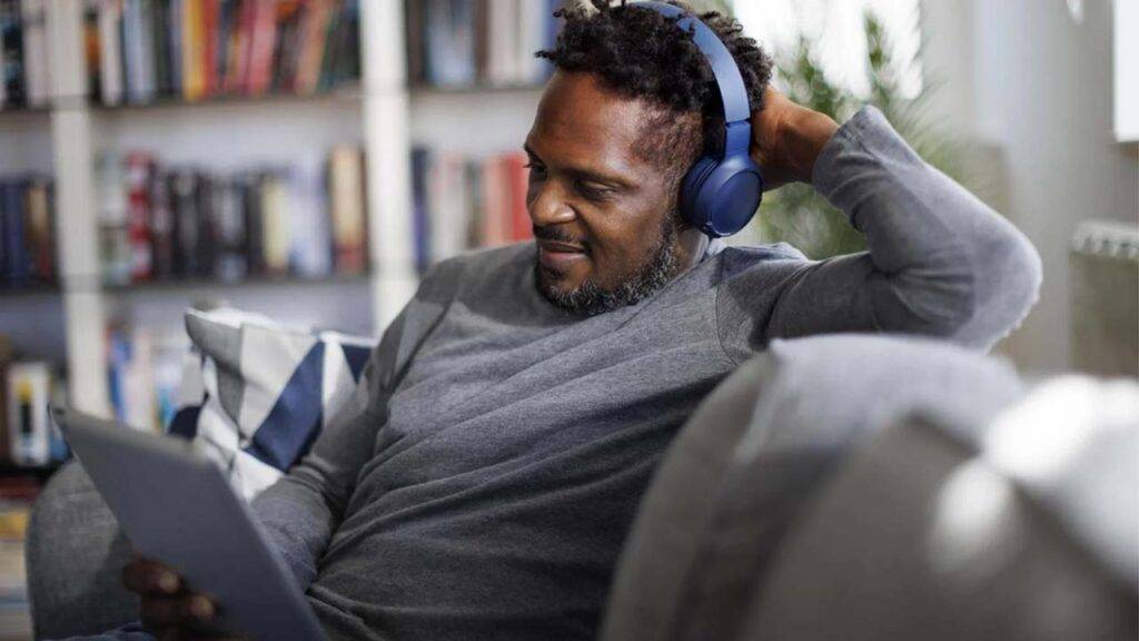 Smiling man with bluetooth headphones watching movie on digital tablet at home